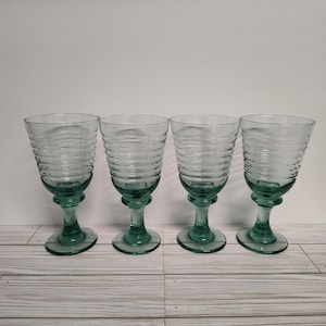 May include: Set of four clear glass wine glasses with a green tint and a ribbed design. The glasses have a round bowl and a stem.