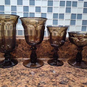 May include: Set of four brown glass goblets with different sizes and shapes. The goblets are on a brown countertop.