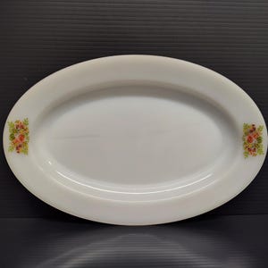 May include: An oval, white serving platter with a floral design on each end. The floral design includes pink, yellow, and orange flowers with green leaves. The platter is made of a smooth, glossy material.