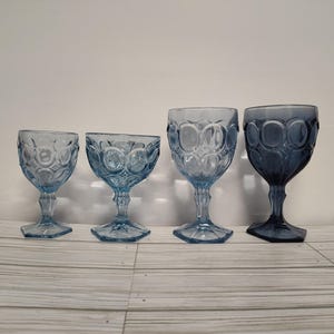 May include: Four blue glass goblets with a textured, bubble-like design. The goblets are arranged in a row from smallest to largest.