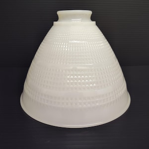May include: A white, cone-shaped lampshade with a textured, geometric pattern. The lampshade has a slightly flared base and a small, cylindrical top. The surface is glossy, reflecting light. The lampshade is designed for use with a lamp.