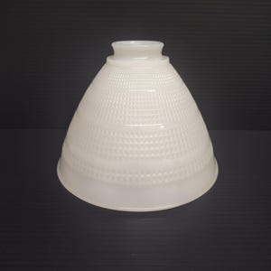 May include: A conical milk glass lamp shade featuring a textured grid pattern across its surface. The shade has a smooth, flared opening at the bottom and a smaller, circular fitter opening at the top, designed for attachment to a light fixture.