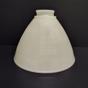 May include: A conical lamp shade made of off-white milk glass featuring a subtle grid pattern across its surface. The shade has a smooth, rounded top opening with a raised collar and a wide, flared bottom edge, creating a classic bell shape.