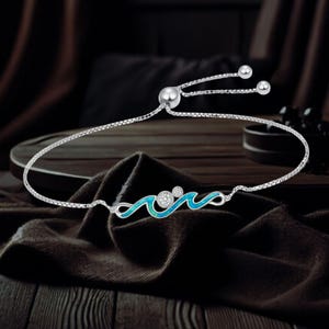 May include: A silver bracelet with a wave design. The wave is outlined in silver and filled with a light blue material. Two clear, round stones are set in the wave design. The bracelet has a sliding clasp for adjustable sizing.