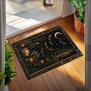 May include: Rectangular doormat with a dark background featuring bats, a crescent moon, and stars. The design includes floral elements in gold and orange, with a decorative border. The mat is placed in front of a white door.
