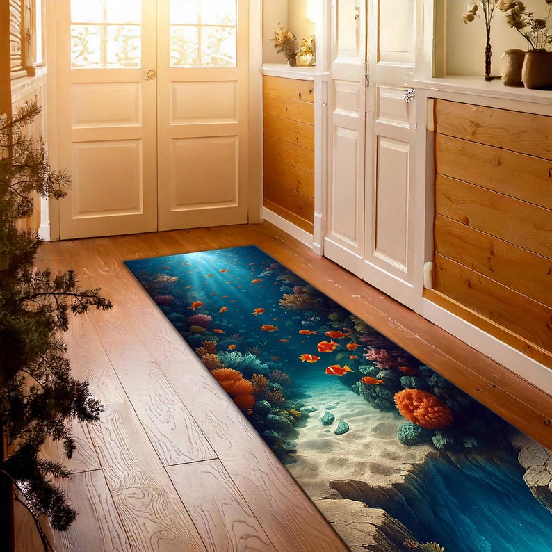 May include: A rectangular rug depicting an underwater scene with coral, fish, and sunlight. The rug's design includes a sandy seabed, vibrant coral reefs, and schools of orange fish swimming in a blue ocean. The rug is placed on a wooden floor.