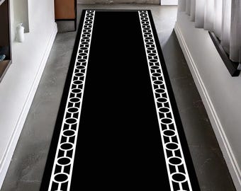 May include: A long, rectangular black rug with a white geometric border. The border design features a repeating pattern of connected ovals and circles. The rug is placed in a hallway setting.