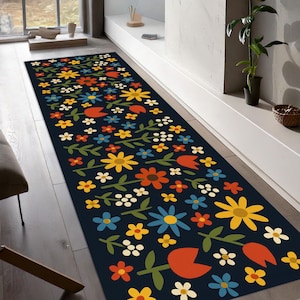 May include: A long, rectangular rug with a dark blue background and a repeating floral pattern. The flowers are in various colours, including yellow, orange, red, blue, and white. Green leaves and stems connect the flowers. The rug is placed on a wooden floor.