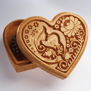 Peut inclure: Une boîte en bois en forme de cœur avec un motif floral gravé sur le couvercle. La boîte est ouverte et l'intérieur est vide.