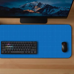 May include: A top-down view of a computer setup featuring a blue mousepad, a black keyboard, and a black mouse. A computer monitor displays a mountain scene. Two potted plants flank the setup on a wooden desk.