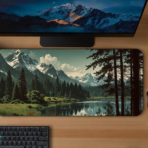 May include: A rectangular mousepad with a scenic mountain landscape design. The image features a lake, trees, and snow-capped mountains in the background. The mousepad has a dark blue, green, and white color scheme.