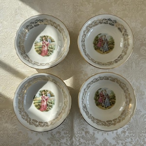 Peut inclure: Quatre bols en porcelaine blanche avec des bords dorés et des motifs floraux dorés décoratifs. Chaque bol présente une image centrale d'une personne dans un paysage. Les bols sont disposés sur une surface à motifs.