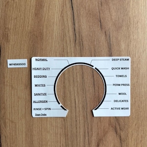 May include: A white appliance control panel with black text on a wooden surface. The panel includes settings like "Normal," "Heavy Duty," and "Deep Steam." The model number "WF45K6500" is also visible.