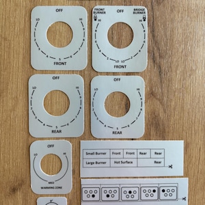 May include: A set of white adhesive stove control labels featuring black text and markings. Includes circular dial surrounds with OFF, LO, HI, and burner positions, plus rectangular strips with burner size charts and the GE Profile logo.