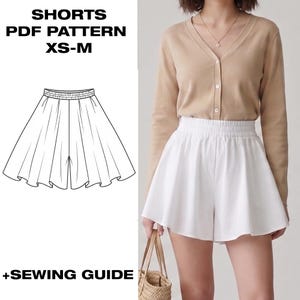 May include: White shorts with an elasticated waistband and a flared design. The image also includes a line drawing of the shorts and text that reads "SHORTS PDF PATTERN XS-M +SEWING GUIDE". A woman is wearing the shorts with a tan cardigan.