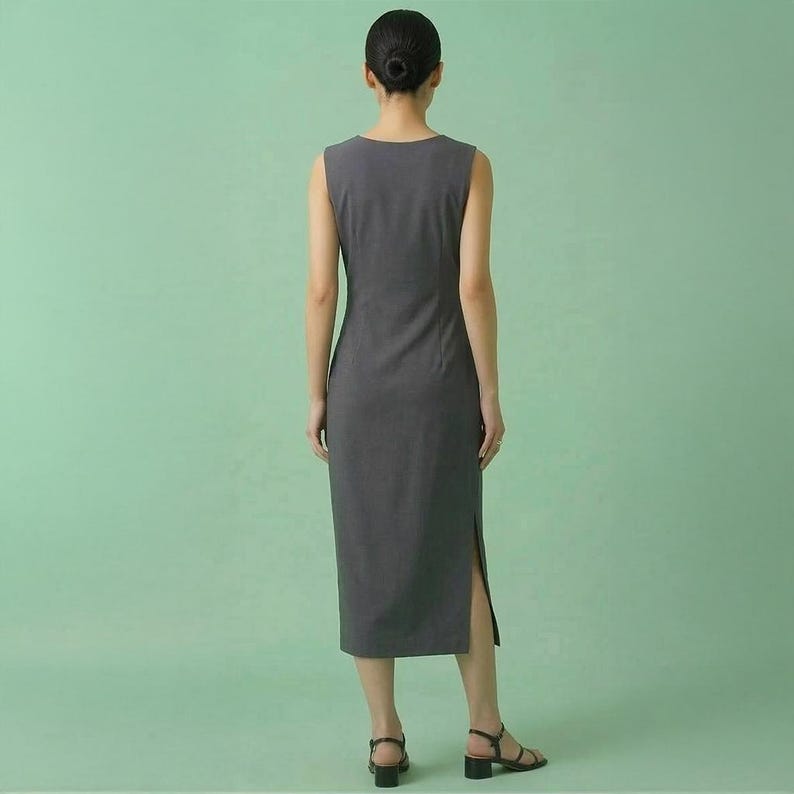Op de afbeelding: Een mouwloze, antracietgrijze jurk met een zoom tot op de knie en zijsplitten. De jurk heeft een eenvoudig, elegant ontwerp en is gemaakt van een gladde stof. Het model draagt zwarte sandalen met een kleine hak.
