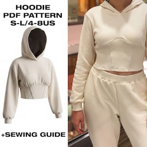 Op de afbeelding: Een crèmekleurige cropped hoodie met een korsetachtig lijfje en lange mouwen. De tekst HOODIE PDF PATTERN S-L/4-8US + SEWING GUIDE is zichtbaar. Het kledingstuk heeft een capuchon met een donkere binnenkant en een gestructureerd taillepaneel.