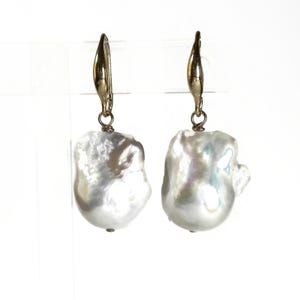 May include: A pair of gold hoop earrings with large, white baroque pearl drops.