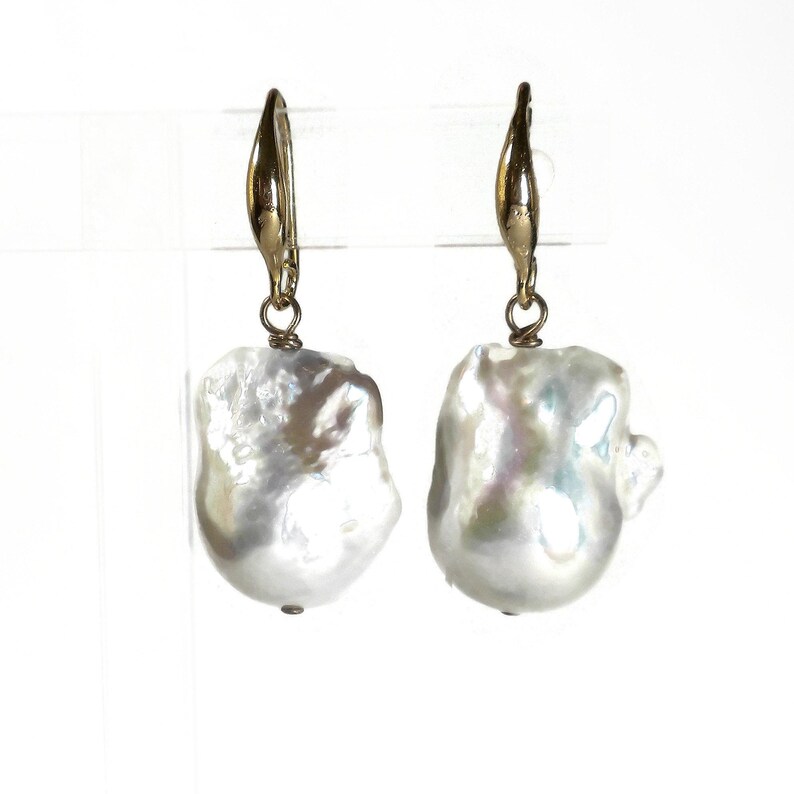 May include: A pair of gold hoop earrings with large, white baroque pearl drops.