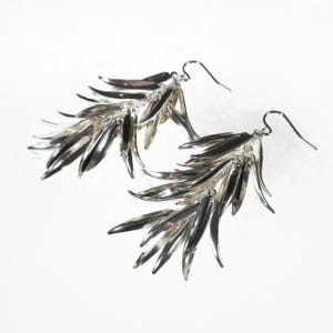 May include: A pair of silver dangle earrings with multiple teardrop-shaped charms. The charms are arranged in a cascading pattern, creating a delicate and elegant look.