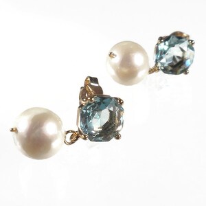 May include: A pair of gold-toned stud earrings. Each earring features a large, round, white pearl and a light blue, square-cut gemstone. The gemstones have multiple facets. The earrings are set against a white background.