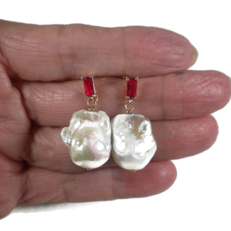 May include: A pair of earrings with large white baroque pearls and red rectangular stones hanging from gold-toned posts.
