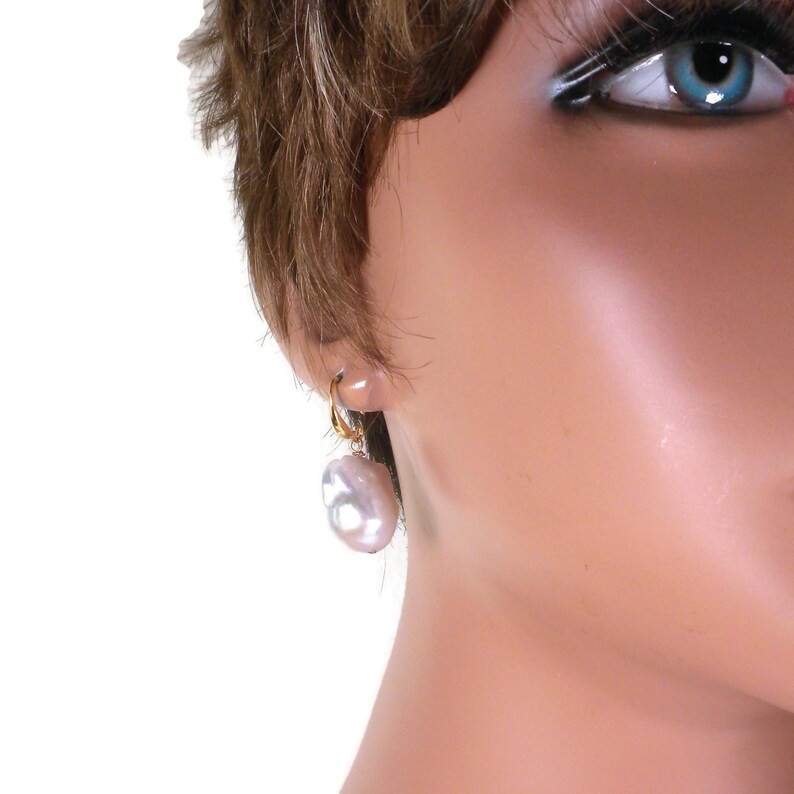 May include: A pair of gold hoop earrings with a large, white baroque pearl dangling from each hoop.