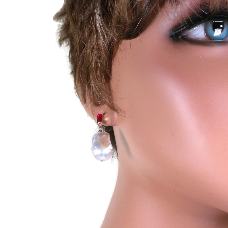 May include: A pair of earrings featuring a large, white baroque pearl with a red gemstone accent.
