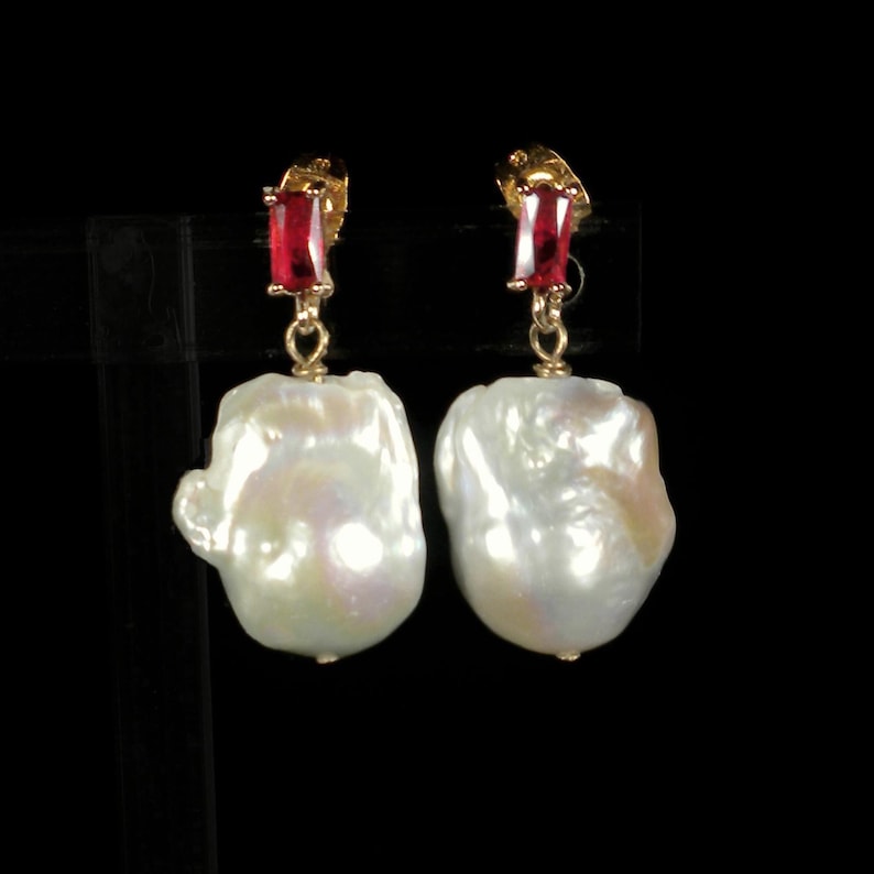 May include: A pair of gold earrings with large white baroque pearls and red gemstone accents.