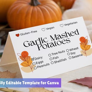 Könnte beinhalten: Eine weiße, gefaltete Karte mit dem Text "Garlic Mashed Potatoes" und Allergeninformationen. Die Karte ist mit herbstlichen Grafiken verziert und befindet sich vor Kürbissen. Der Text "Fully Editable Template for Canva" befindet sich unten.