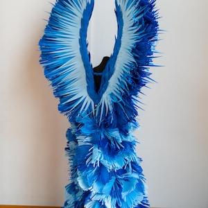 May include: A blue and white paper dress with a ruffled design. The dress is made of many layers of paper, creating a voluminous and textured look.