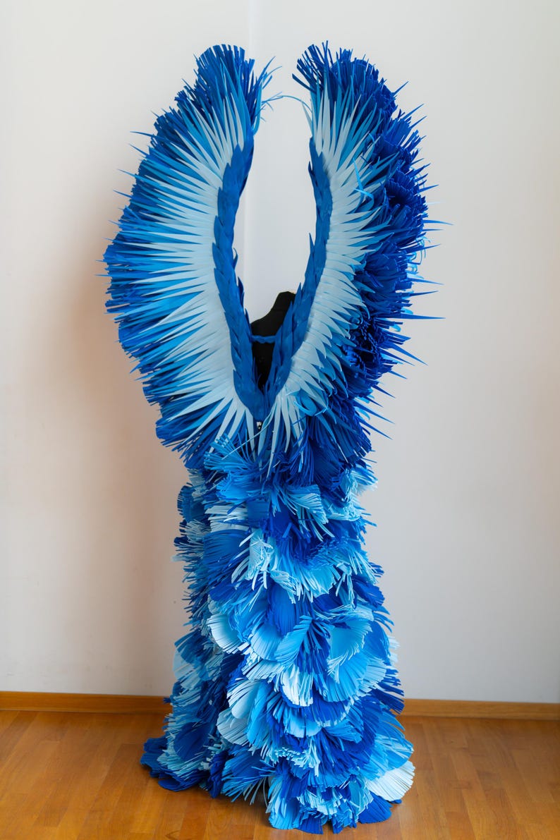 May include: A blue and white paper dress with a ruffled design. The dress is made of many layers of paper, creating a voluminous and textured look.