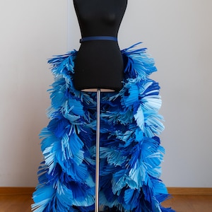 May include: A black dress form with a blue belt and a skirt made of blue paper fringe.