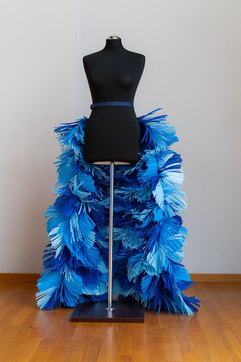 May include: A black dress form with a blue belt and a skirt made of blue paper fringe.