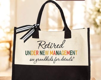 May include: A canvas tote bag with black handles and a black bottom panel. The bag features the text "Retired UNDER NEW MANAGEMENT see grandkids for details" in various colors. A black and white striped bow adorns one handle.