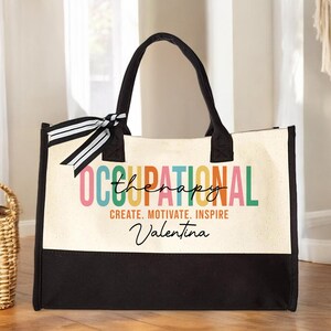 May include: A black and white canvas tote bag with a colorful "Occupational Therapy" design. The text "Create. Motivate. Inspire" is printed below the design, and the name "Valentina" is written in cursive below the text.
