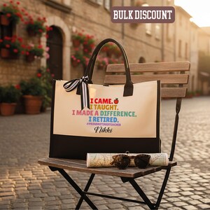 Puede incluir: Bolso tote color crema con asas y base negras. El bolso muestra el texto "I CAME. I TAUGHT. I MADE A DIFFERENCE. I RETIRED." con un gr&aacute;fico de manzana. Un lazo a rayas blanco y negro est&aacute; atado al asa.