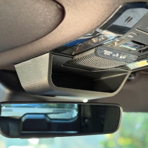 Könnte beinhalten: Innenaufnahme eines Autos mit einer schwarzen Dachkonsole mit Ablage, Knöpfen und einem Rückspiegel. Die Konsole ist an einem dunkelgrauen Dachhimmel befestigt. Der Spiegel reflektiert die Außenumgebung.