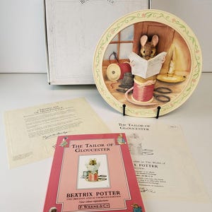 May include: A decorative plate from "The World of Beatrix Potter" featuring a mouse reading a newspaper titled "The Tailor of Gloucester." The plate is displayed with a book, certificate, and box. The plate has a cream-colored border with floral accents.