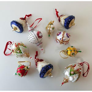 May include: A collection of nine decorative ornaments featuring various shapes including spheres and bells. These ornaments are adorned with intricate beadwork, sequins, and metallic accents in colors of red, blue, white, gold, and green, each with a hanging loop.