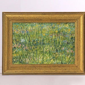 May include: A framed artwork featuring a vibrant field of tall green grass and wildflowers in shades of yellow, pink, and blue. The painting is enclosed in a gold-colored, ornate frame, adding a touch of elegance to the pastoral scene.