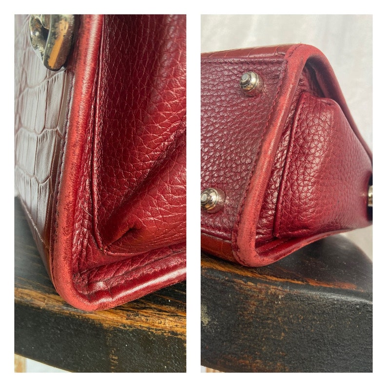 May include: Close-up of a red leather handbag with silver hardware. The bag has a textured finish and a slightly worn look.