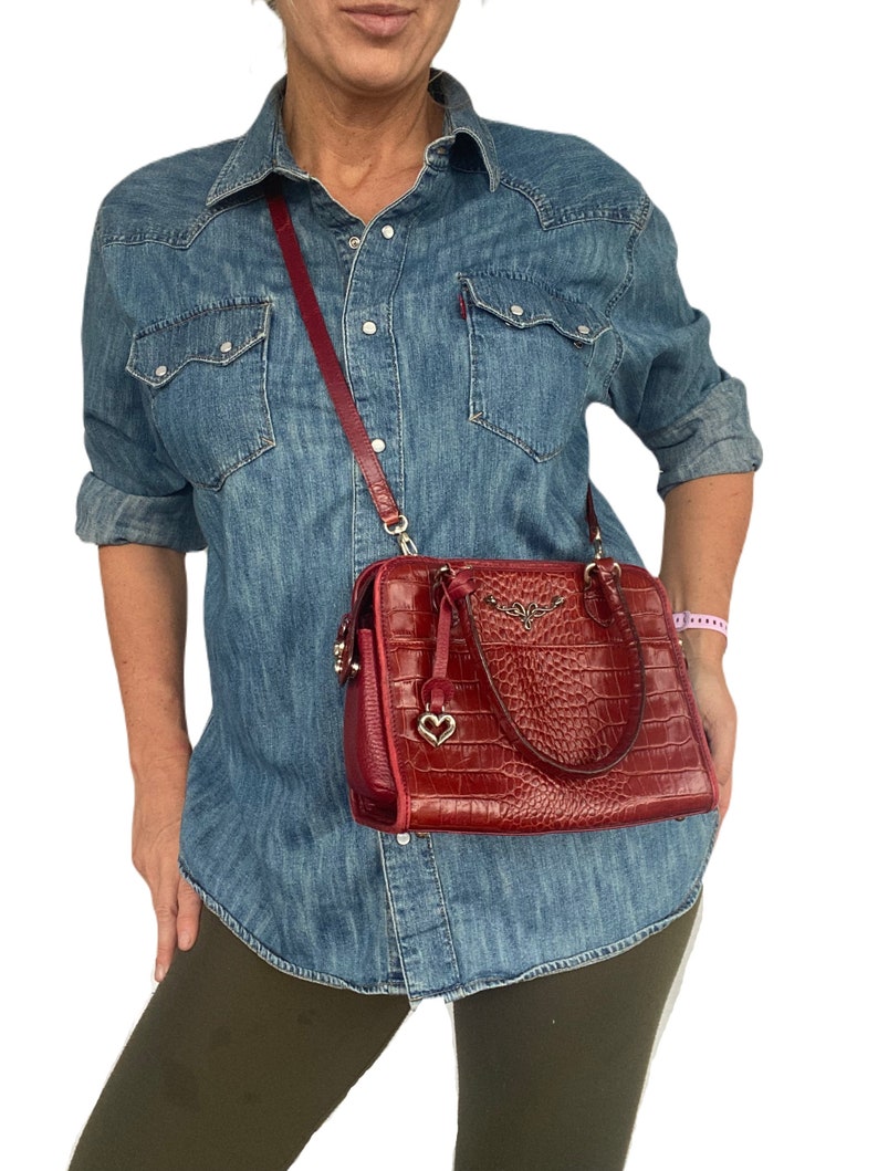 May include: A red leather handbag with a crocodile embossed pattern and a gold heart charm. The bag has a top handle and a long shoulder strap.