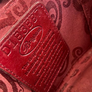 May include: A red leather tag with the text "Dooney & Bourke" and "The Brighton Collection Handmade of the finest leather & materials.  Genuine Leather.  Made in China.  Style # 150001100" printed on it.