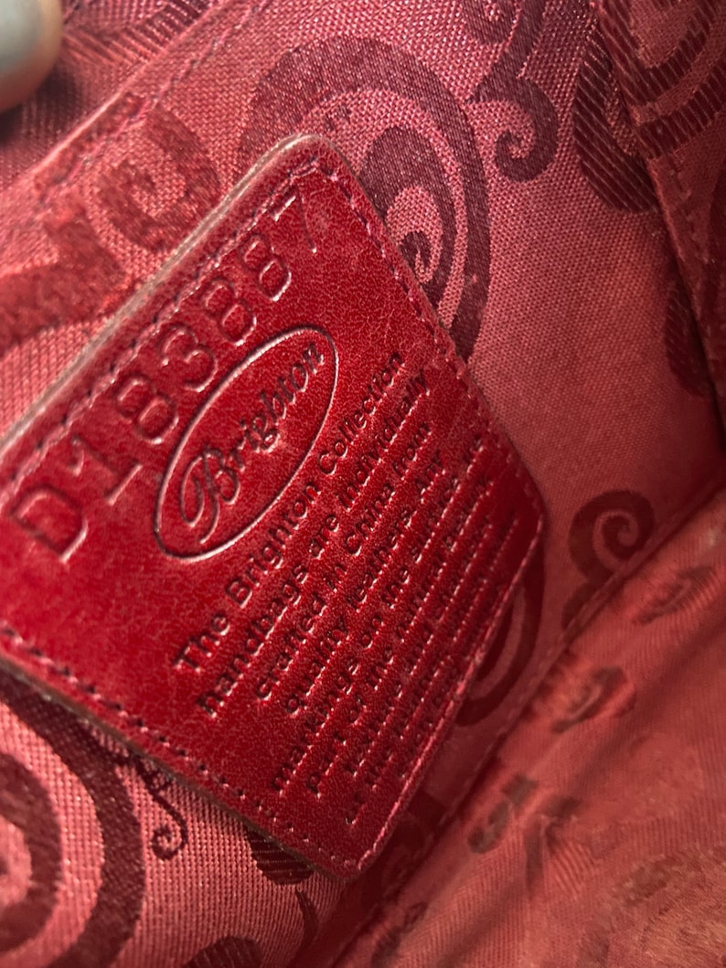 May include: A red leather tag with the text "Dooney & Bourke" and "The Brighton Collection Handmade of the finest leather & materials.  Genuine Leather.  Made in China.  Style # 150001100" printed on it.