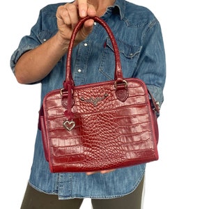 May include: A red crocodile embossed leather handbag with a gold heart charm and a gold winged logo.
