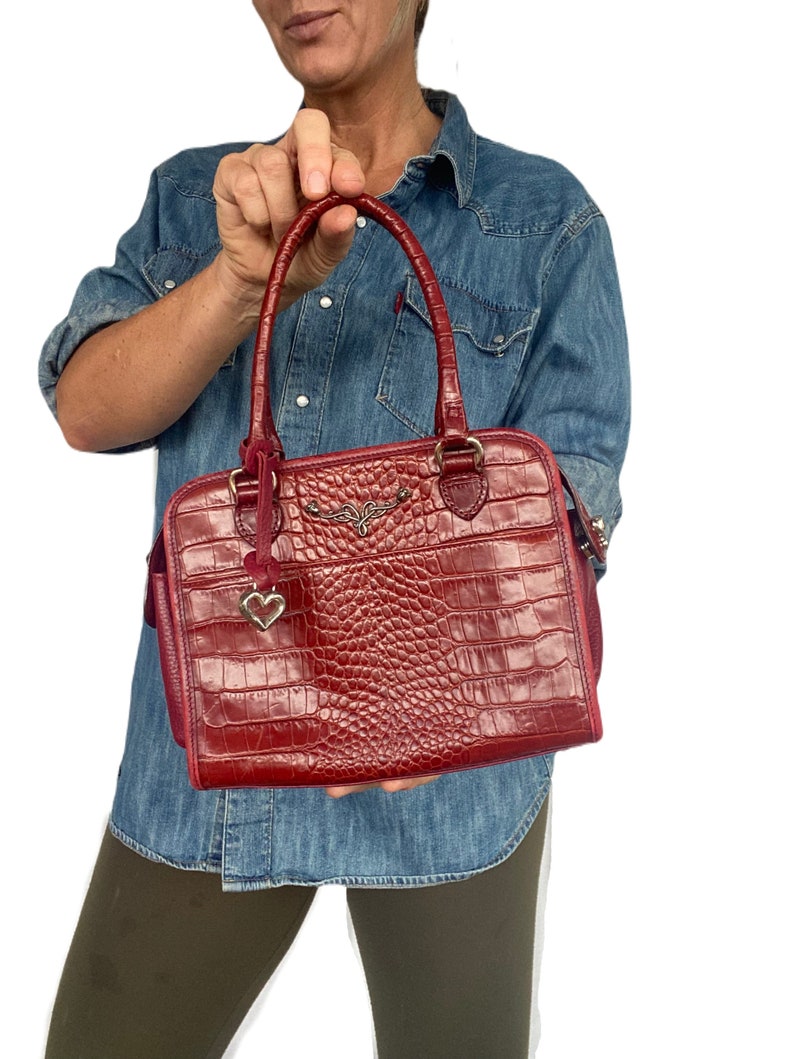 May include: A red crocodile embossed leather handbag with a gold heart charm and a gold winged logo.