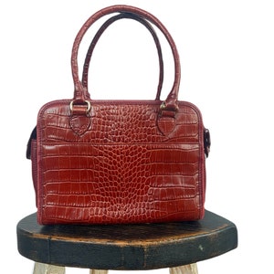 May include: A red leather handbag with a crocodile-embossed pattern. The bag has two top handles and a zipper closure.