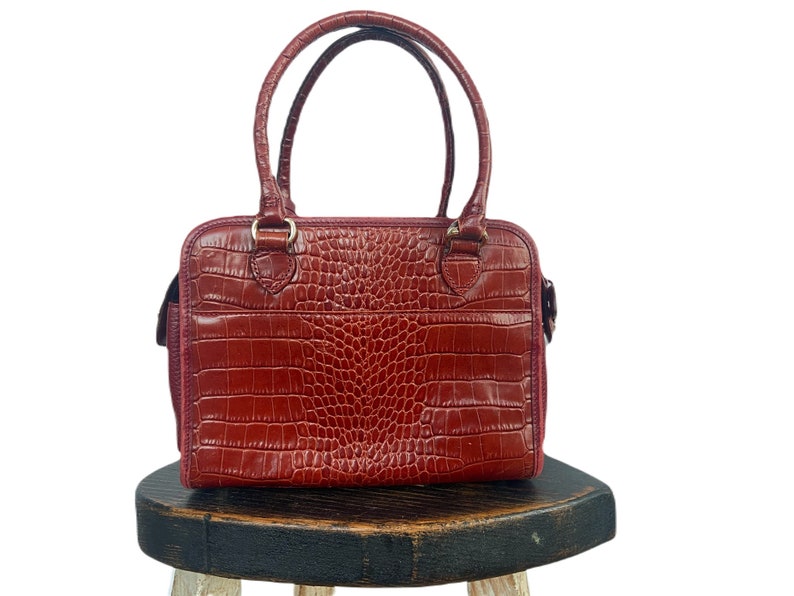May include: A red leather handbag with a crocodile-embossed pattern. The bag has two top handles and a zipper closure.