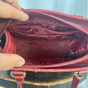 May include: A red leather handbag with a zipper closure and a patterned lining. The bag has a top handle and a shoulder strap.